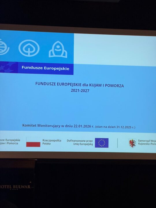 Widok na ekran projekcyjny, na którym widnieje slajd z napisem „Fundusze Europejskie dla Kujaw i Pomorza 2021-2027